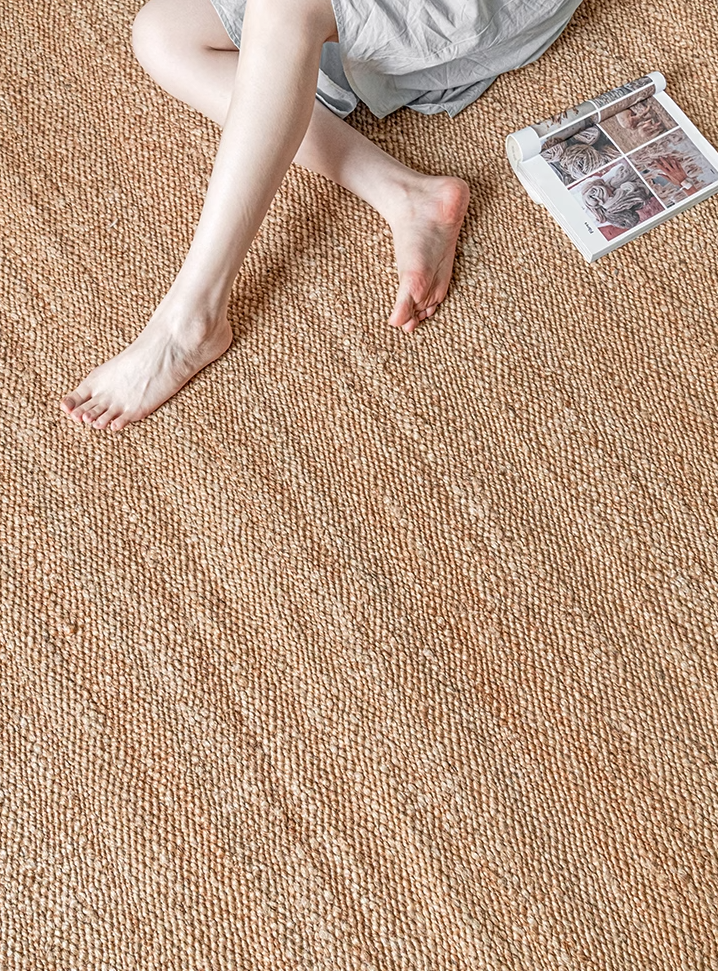 A close-up shot of a hand holding and folding a natural fiber rug, highlighting its texture and weave.