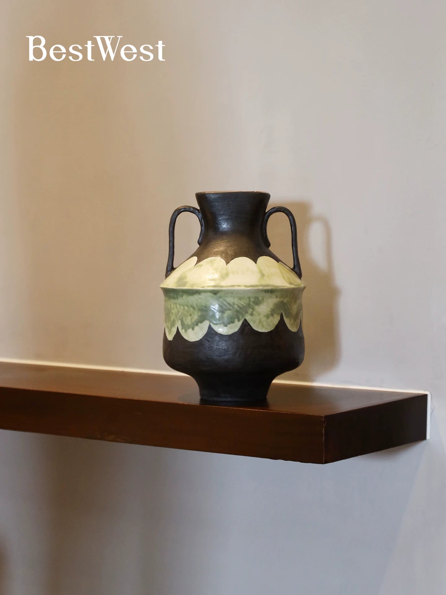 Handmade ceramic vase with black body and green scalloped detail displayed on a minimalist wooden shelf