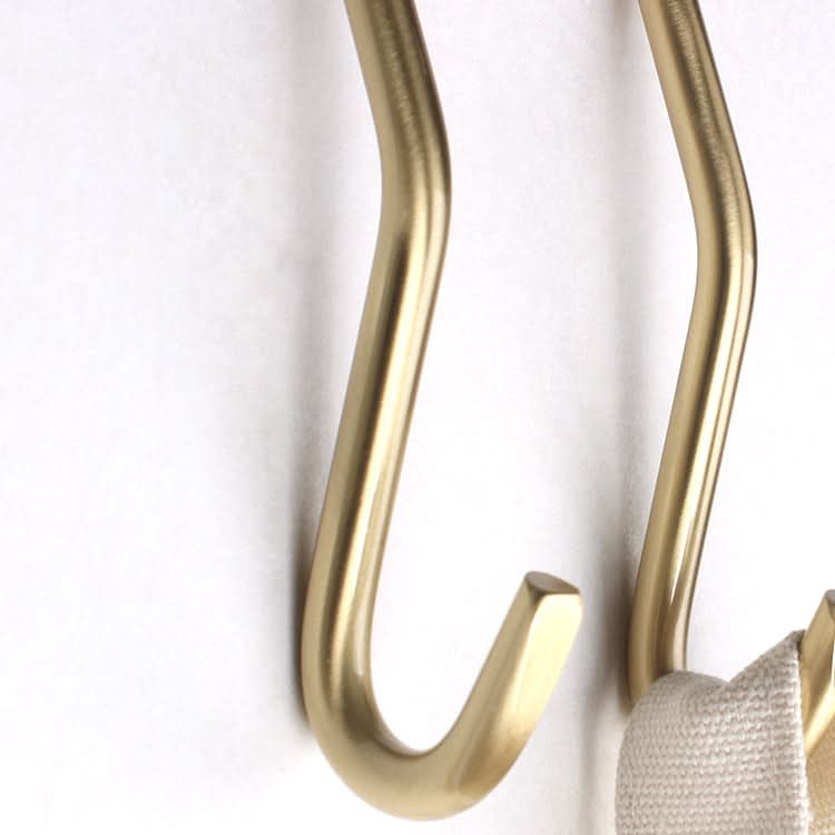 Minimalist brass wall hooks with a cream fabric loop hanging on one.