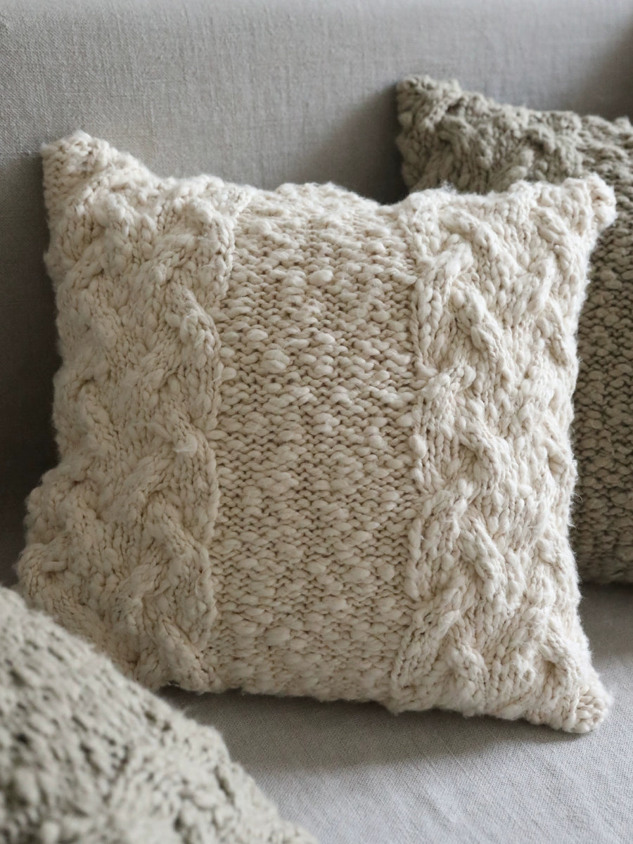 Cream knitted throw pillows with cable knit texture on sofa. Cozy decor set of 4.