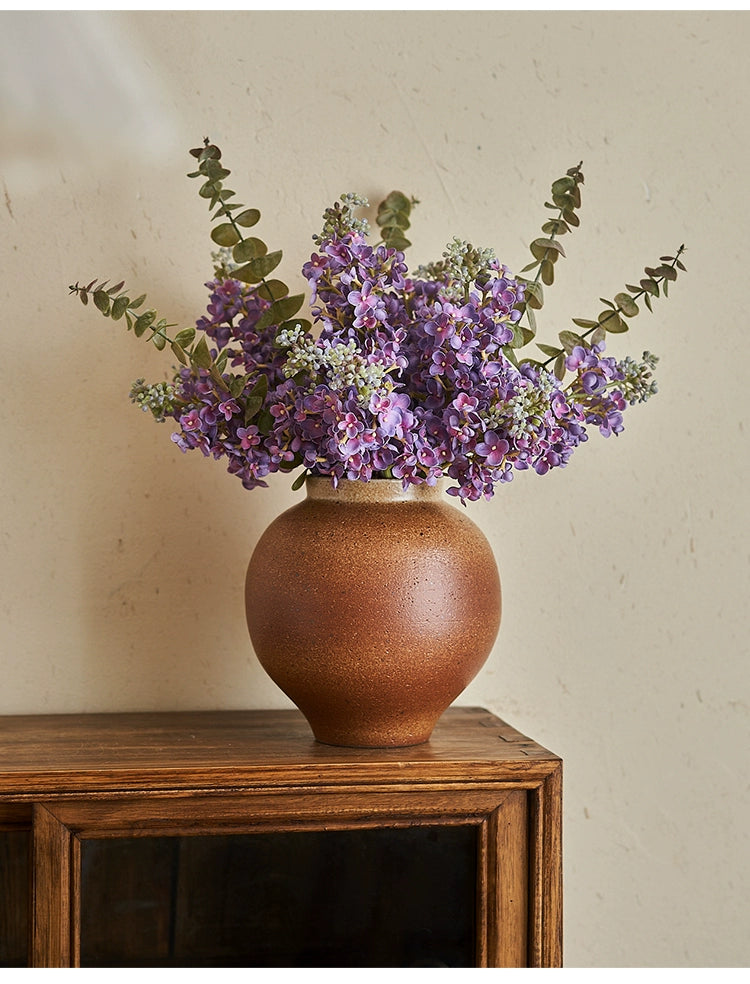 Rustic brown handmade vase with purple flowers.  Handmade pottery vase, rustic brown glaze, displaying purple flowers.