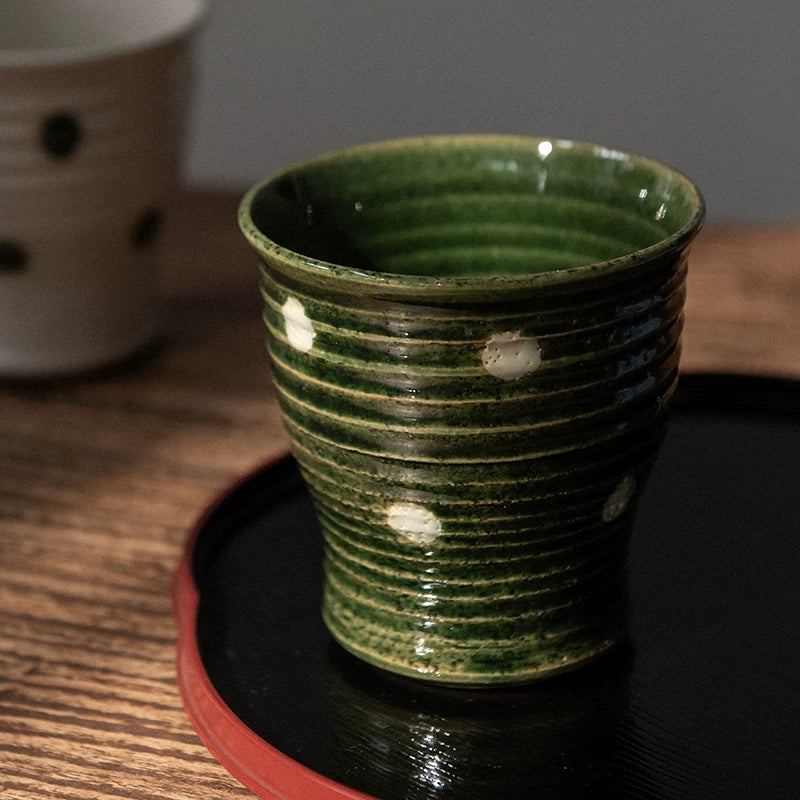 Close-up of a dark green ceramic Yunomi cup with white polka dots, resting on a black and red lacquer tray.