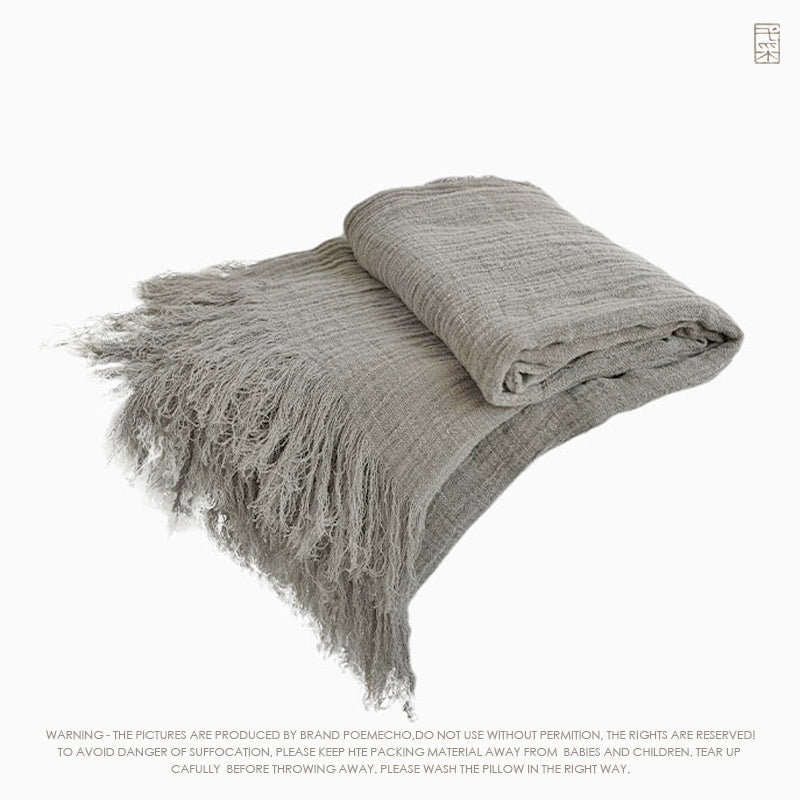 Light gray linen throw blanket with textured weave and delicate fringes.  Rustic style.