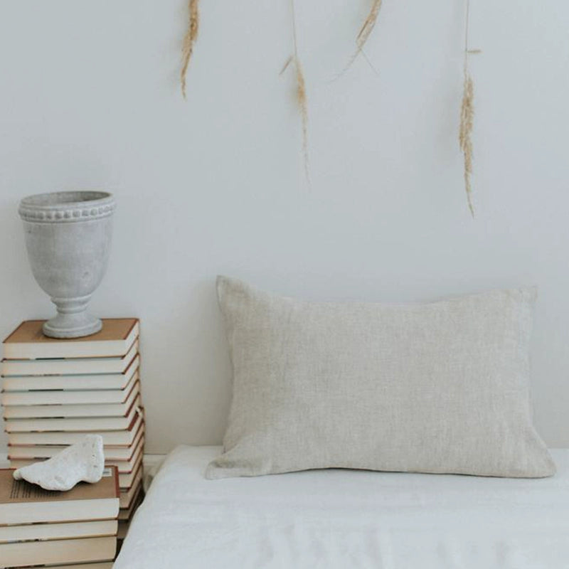 Elegant linen pillow case with frills, light neutral color, on a white bed.