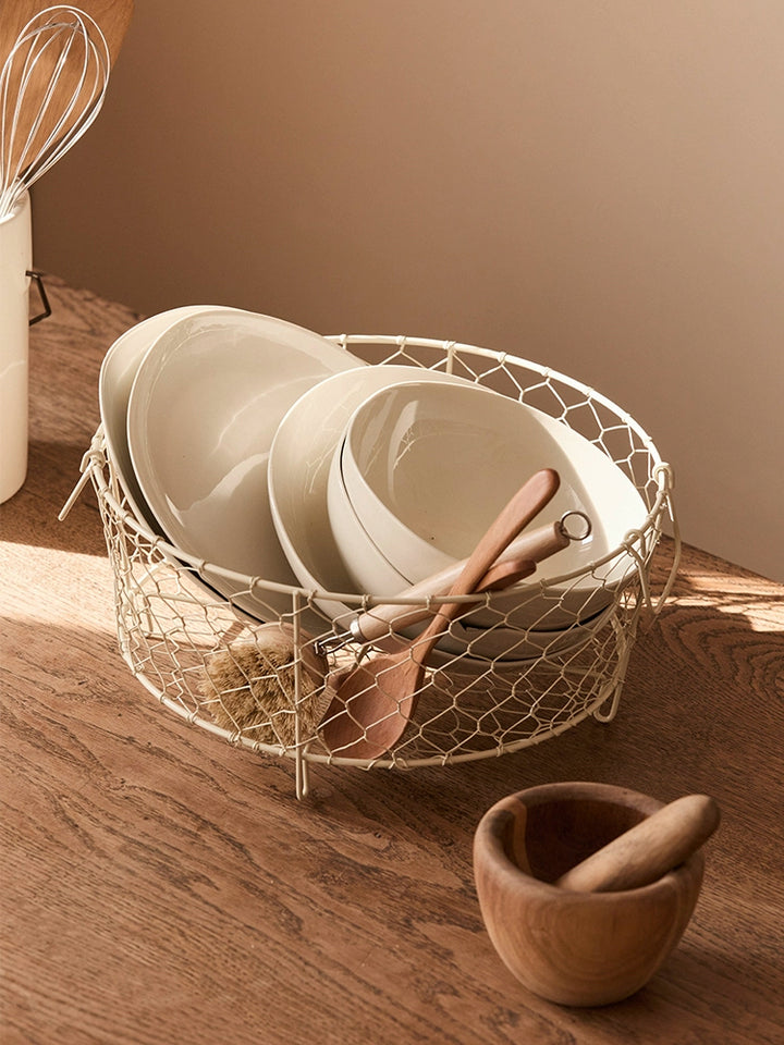 Beige wire dish basket with handles, holding dishes and utensils.  Rustic, wire design. Kitchen storage.