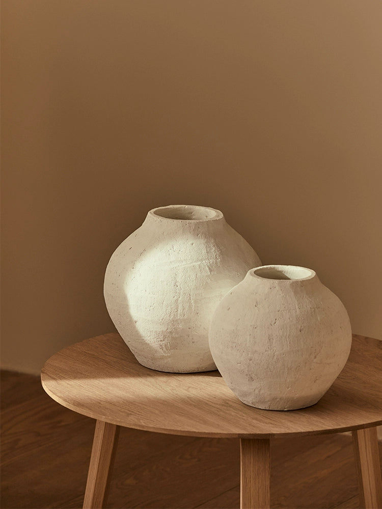 Two textured white ceramic vases on a light brown wooden coffee table.