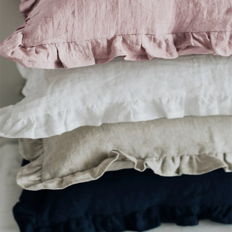 Stack of elegant linen pillow cases in rose, white, natural, and navy, featuring frill details.