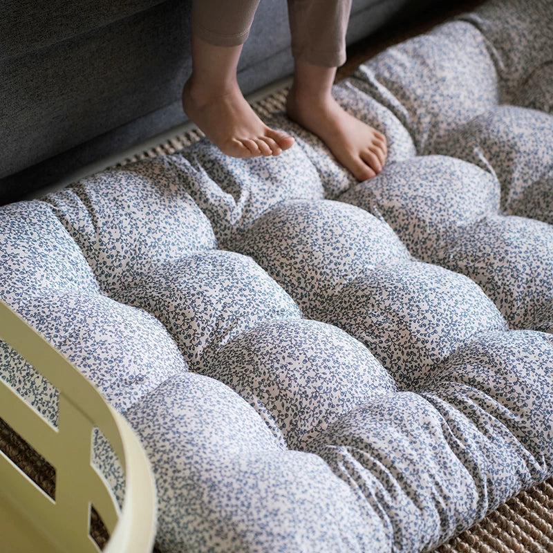 Close-up of a greyish-blue tufted floor cushion with child's bare feet standing on it.