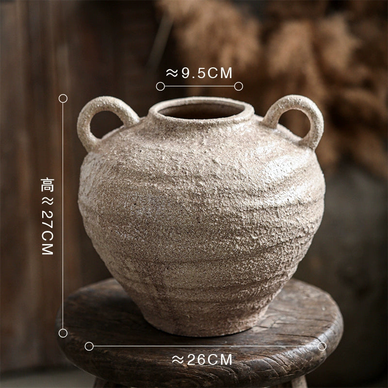 Rustic ceramic vase with handles on wooden stool, textured decorative pottery, home decor accent.