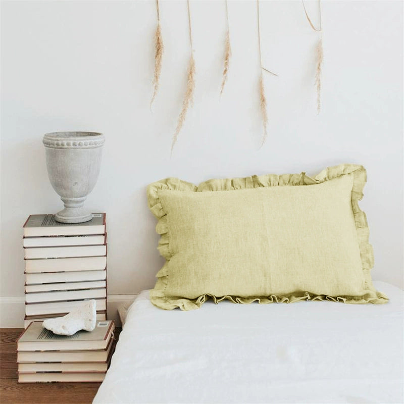 Light yellow linen pillow cases with frills on a bed, next to stacked books.