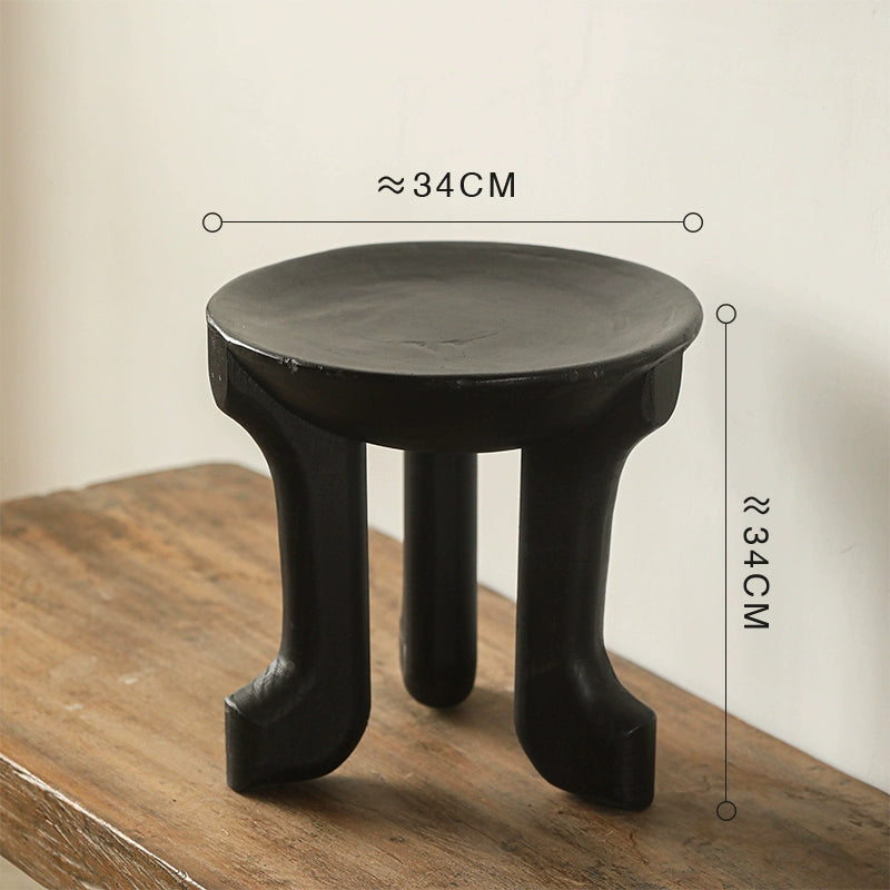 Ethnic style black wooden side table, round coffee table with curved legs on rustic wood.