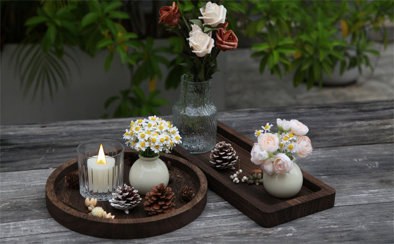 Dark wood decorative tray with candle, pinecones, and floral arrangements.