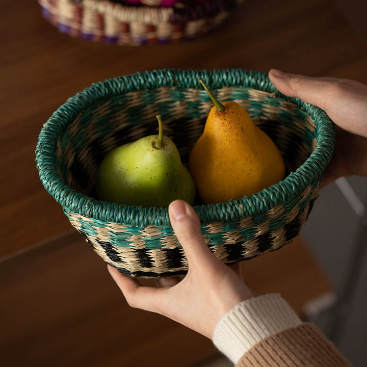 Hands holding a small, round woven seagrass basket filled with green and yellow pears.
