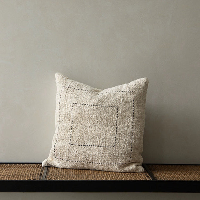 Beige woven boho throw pillow with black stitching, part of a living room set.