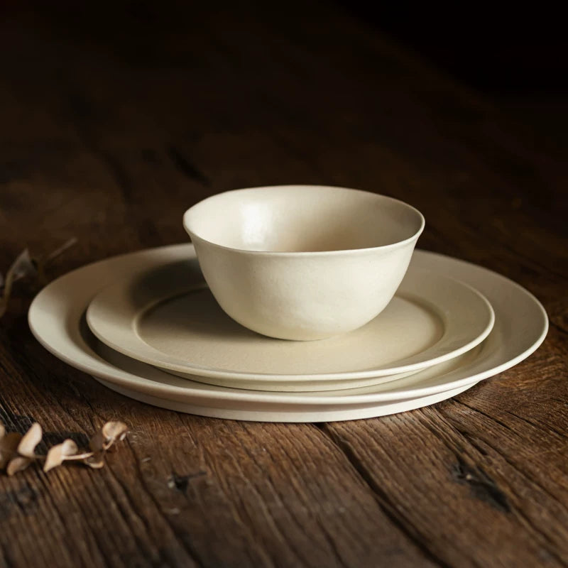 Cream white ceramic bowl stacked on two matching plates on a dark wooden table.