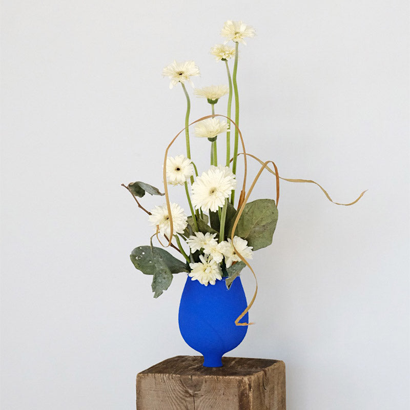 Klein Blue Flower Vase: Handcrafted ceramic vase with white flowers on a wooden pedestal.