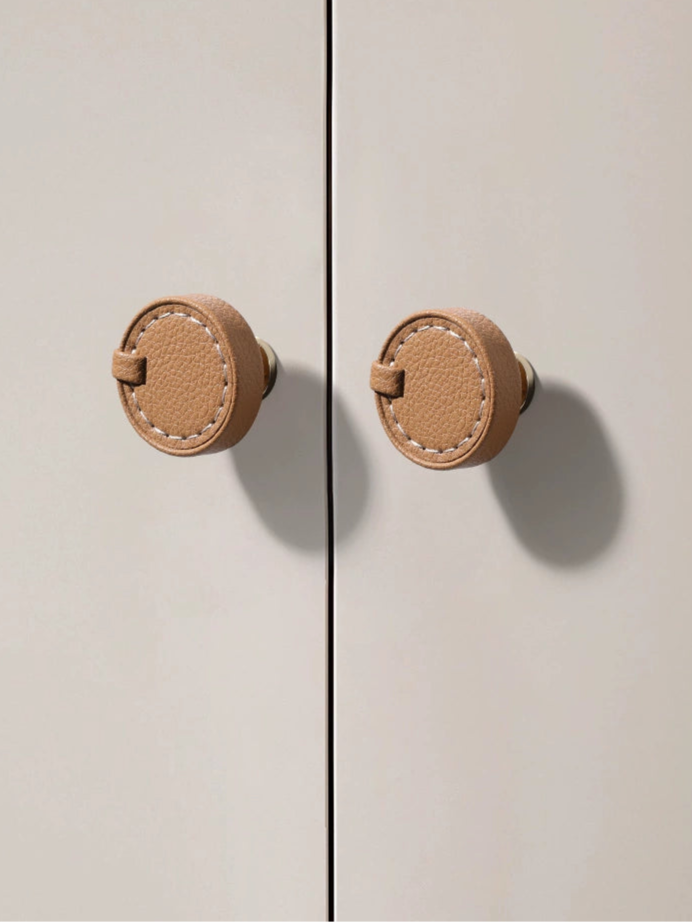 Tan leather round drawer pulls & cabinet knobs with white stitching on a light gray cabinet.