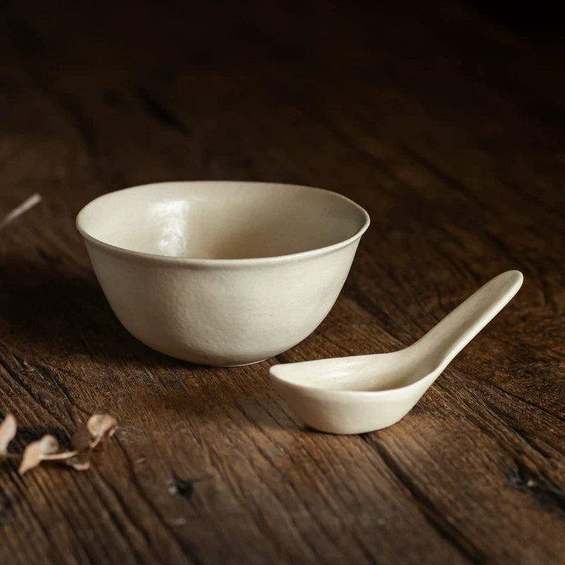 Cream white ceramic bowl paired with a matching long-handled spoon on a dark wood surface.