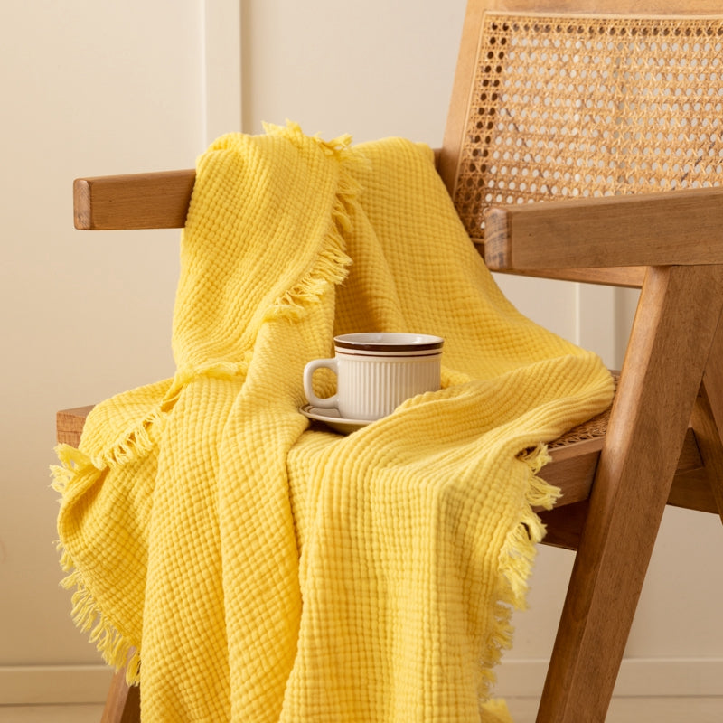 Olive green waffle weave throw blanket draped over a wooden chair.  Fringed edges.  Small white cup on a saucer.