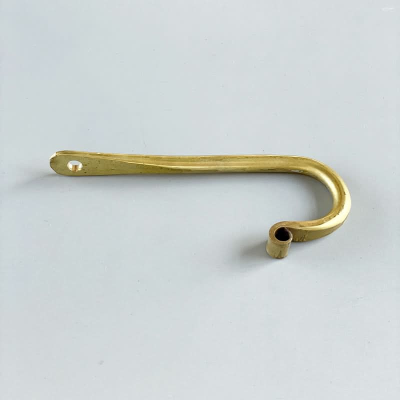 Gold J-shaped wall hook made of brass with a hole for mounting on a light grey background.