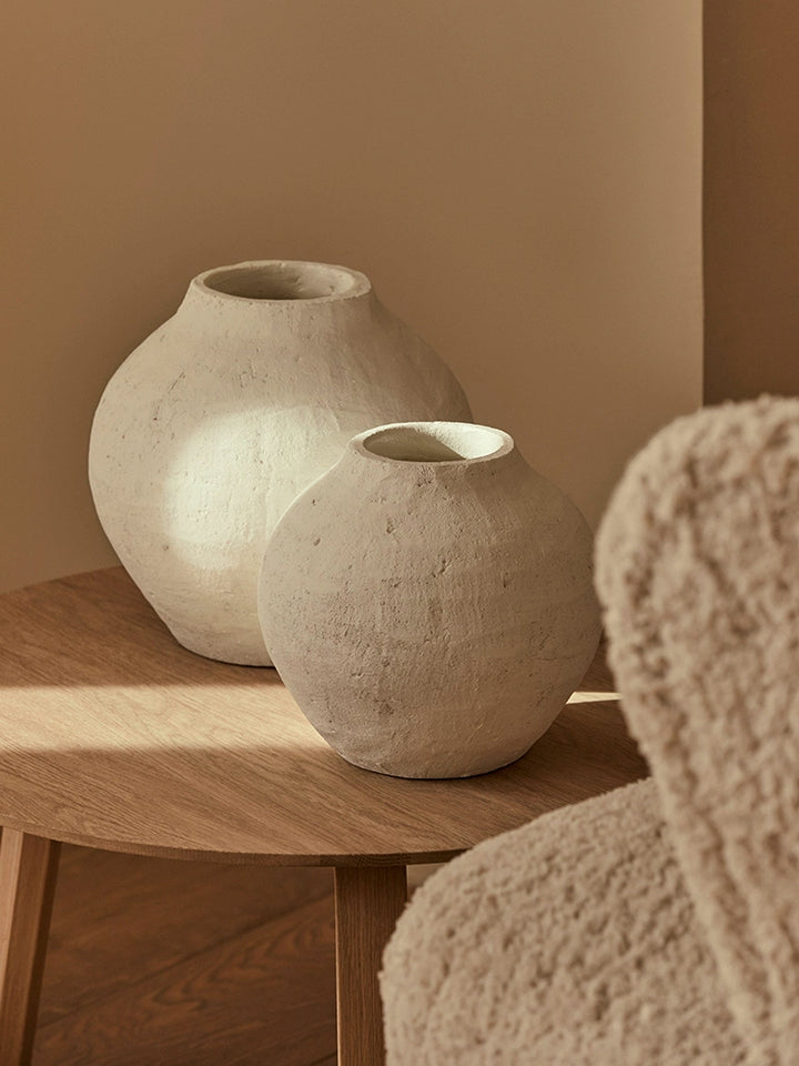 Two white terracotta-style vases, decorative home decor, on a light oak wooden table.  Vases are textured and have a slightly distressed look.