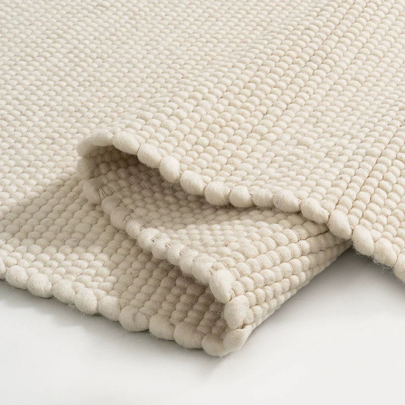 Cream white textured woven rug folded showing detailed pebble-like weave and soft texture.