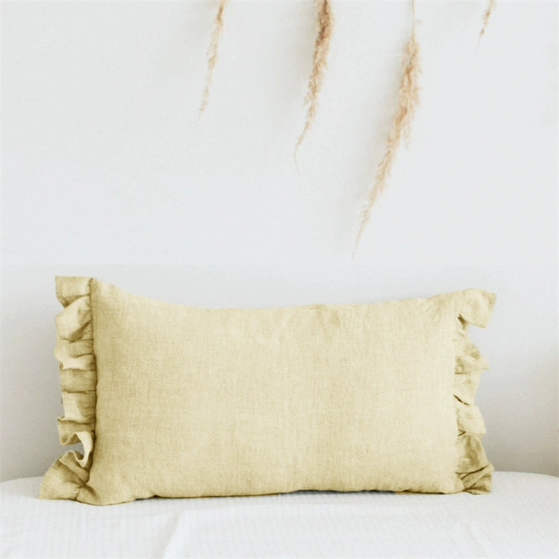 Elegant linen pillow case in pale yellow with delicate frills on a white textured surface.