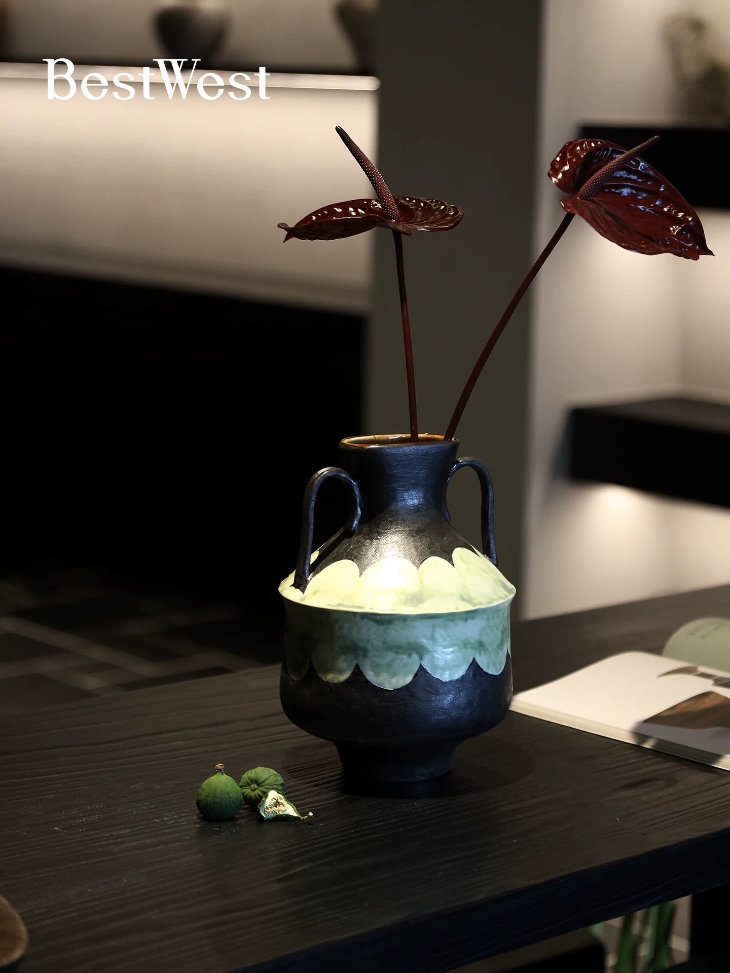 Decorative black and green ceramic vase with two handles styled with floral stems on a black table