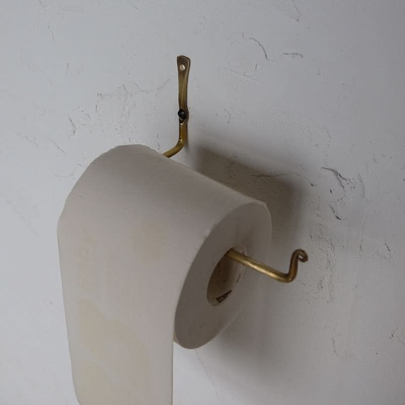 Gold toilet paper holder with roll on textured white wall.