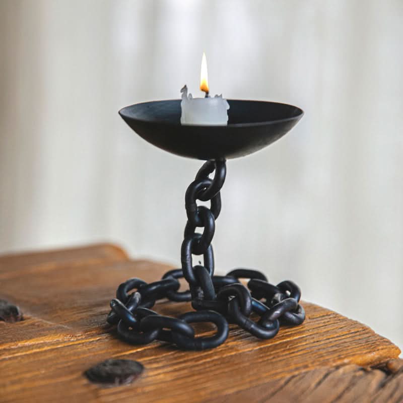 Black chain candle holder with lit candle on rustic wooden table.