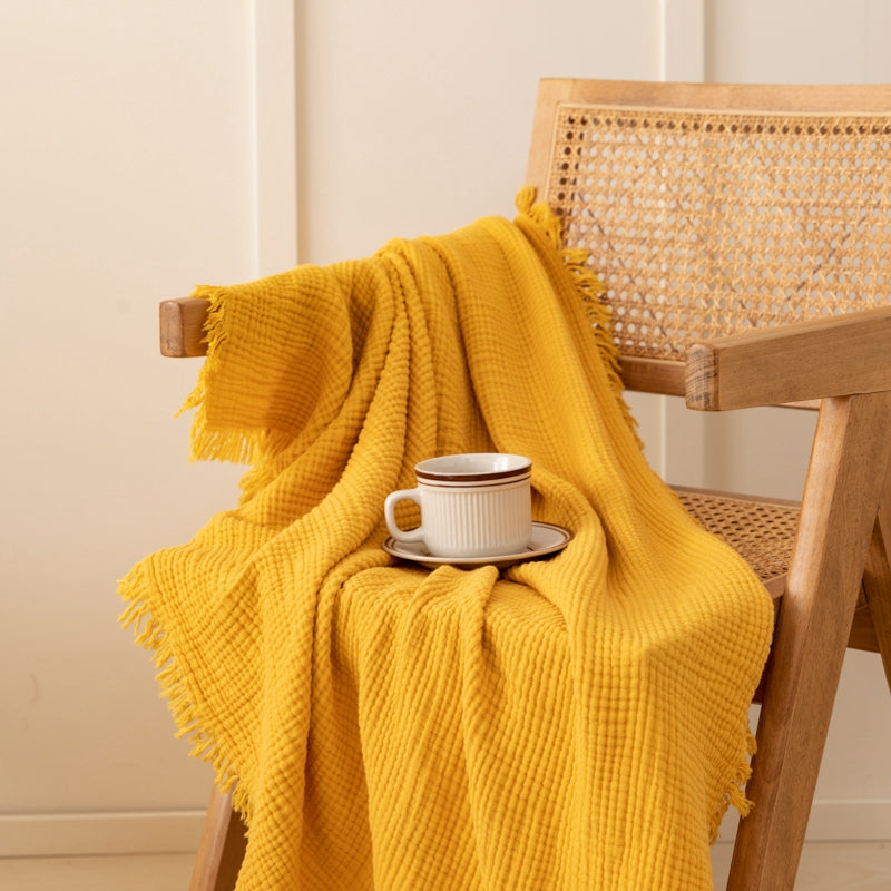 Olive green waffle weave throw blanket draped over a wooden chair.  Fringed edges.  Small coffee cup on a saucer.