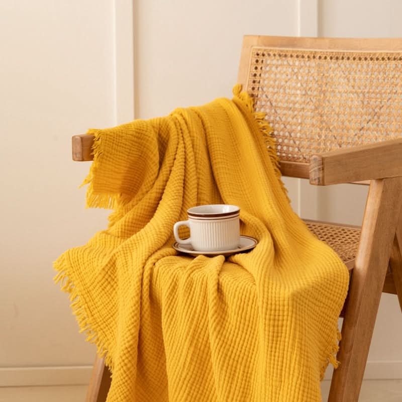 Yellow four-layer waffle weave cotton throw blanket draped on a wooden chair with a coffee cup.