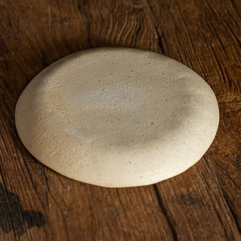 Underside view of a rough, unglazed, cream-colored ceramic plate showing its textured bottom.