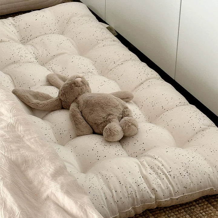 Cream colored floor cushion with black speckles, a plush bunny toy lying on top.