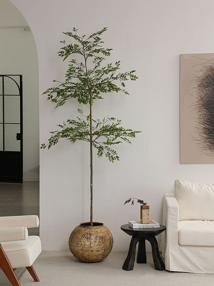 Rustic wooden side table with black tripod legs next to a white sofa and a potted plant.