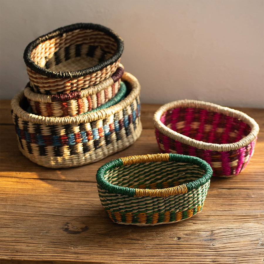 Stack of woven seagrass baskets with colorful bands in green, pink, and brown tones on a wooden surface.