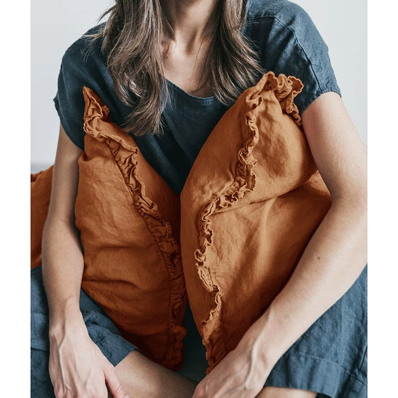 Rustic linen pillowcases in burnt orange with frills, held by a person in a blue shirt.