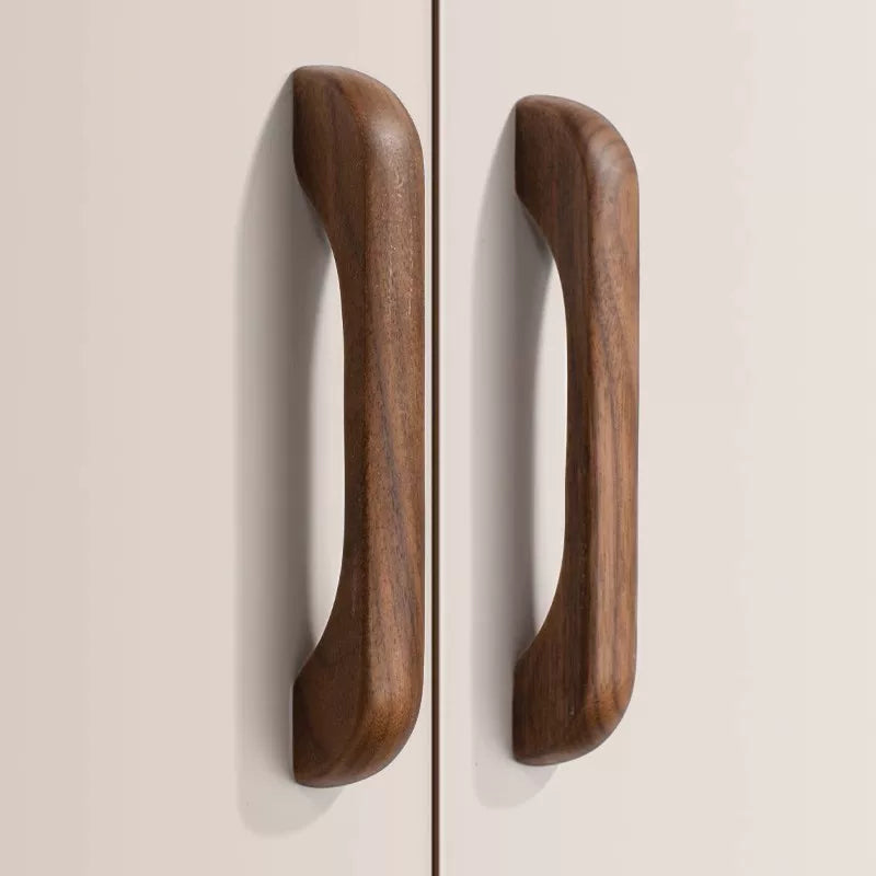 Two curved, elongated walnut wood drawer pulls installed vertically on a beige cabinet door.