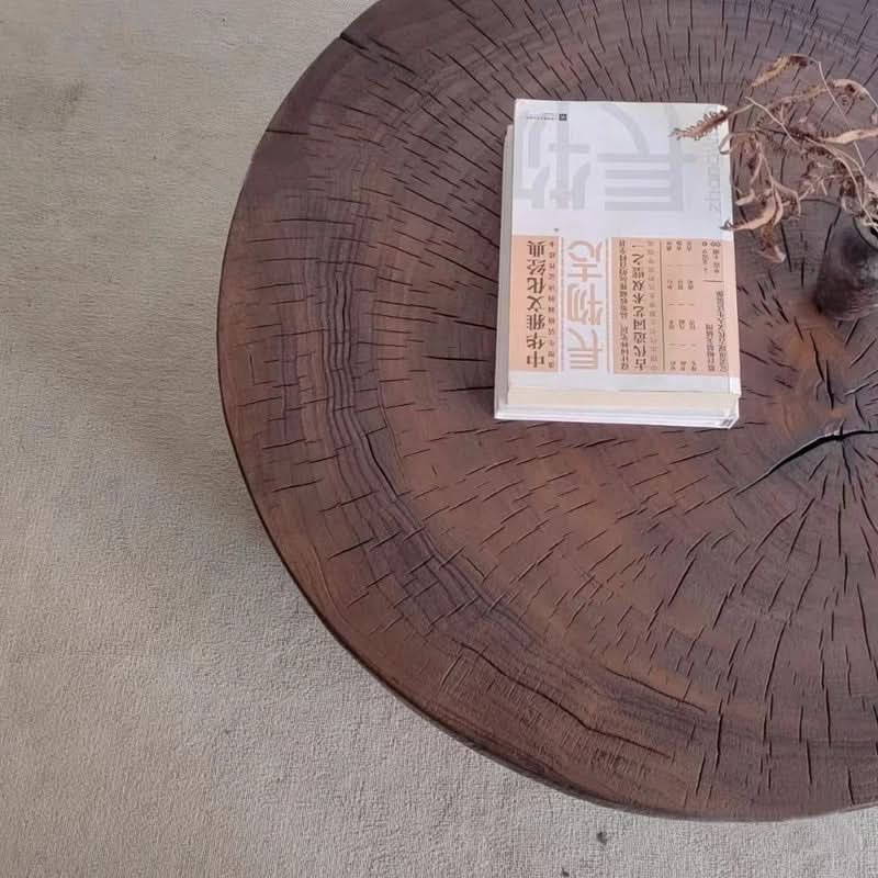 Raw wood coffee table with rustic texture, featuring a stack of books and dried plant decor.