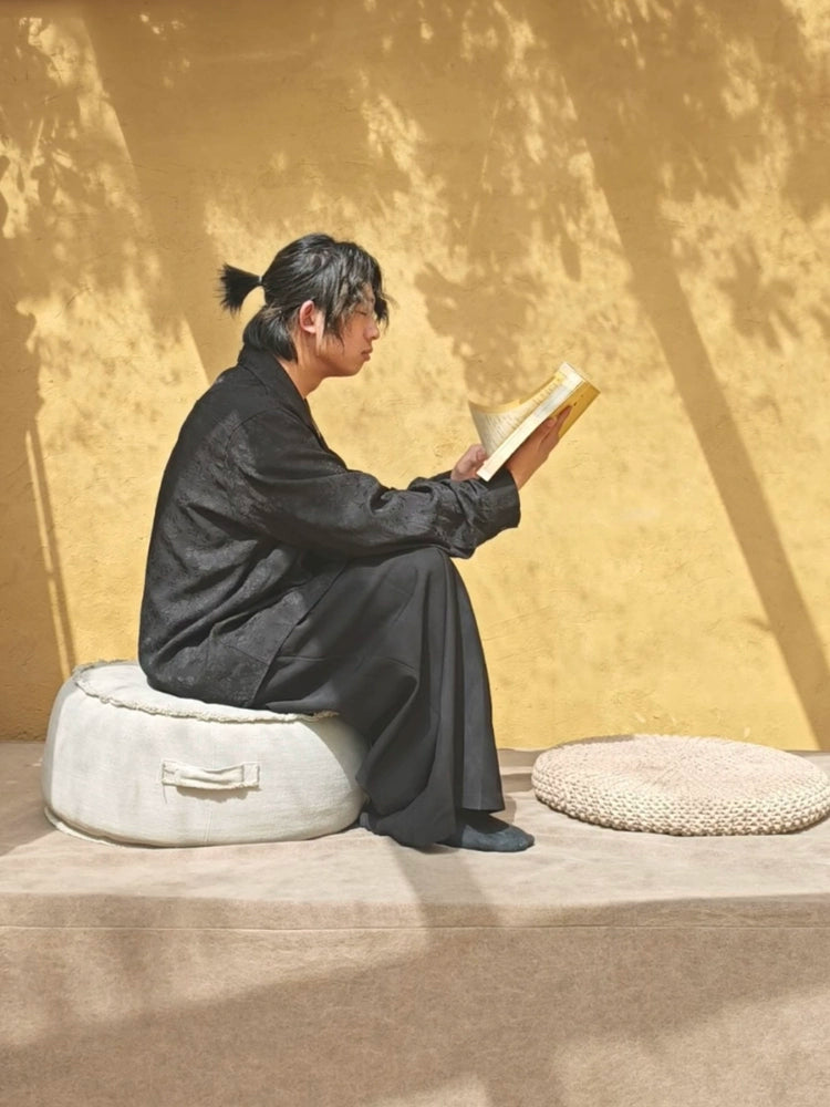 Round beige fabric ottoman pouf with handle, decorative accent seating for living room or bedroom.