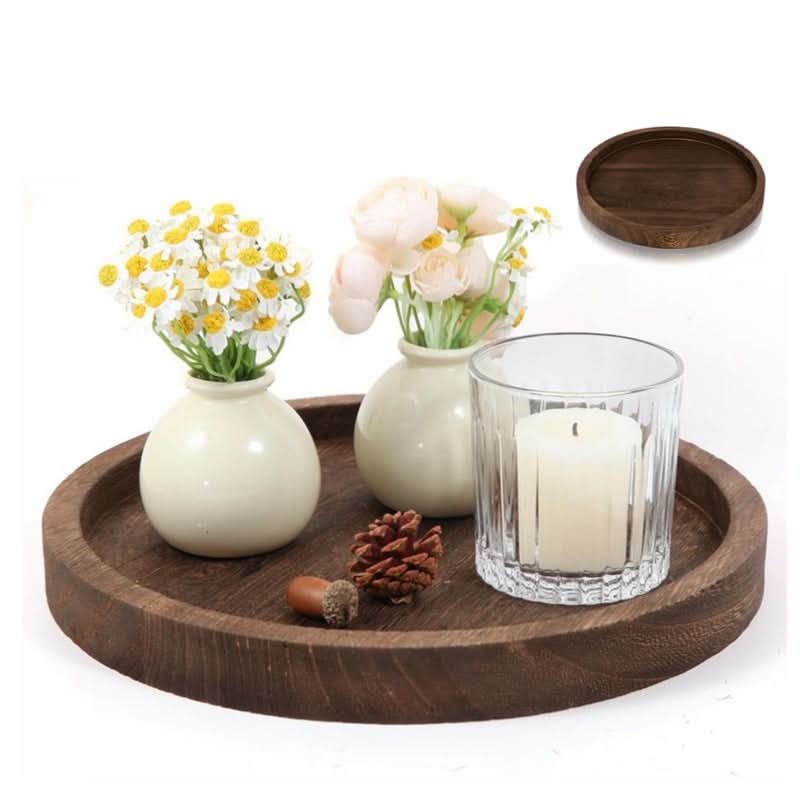 Round dark wood decorative tray with white vases, flowers, candle, and pinecones.