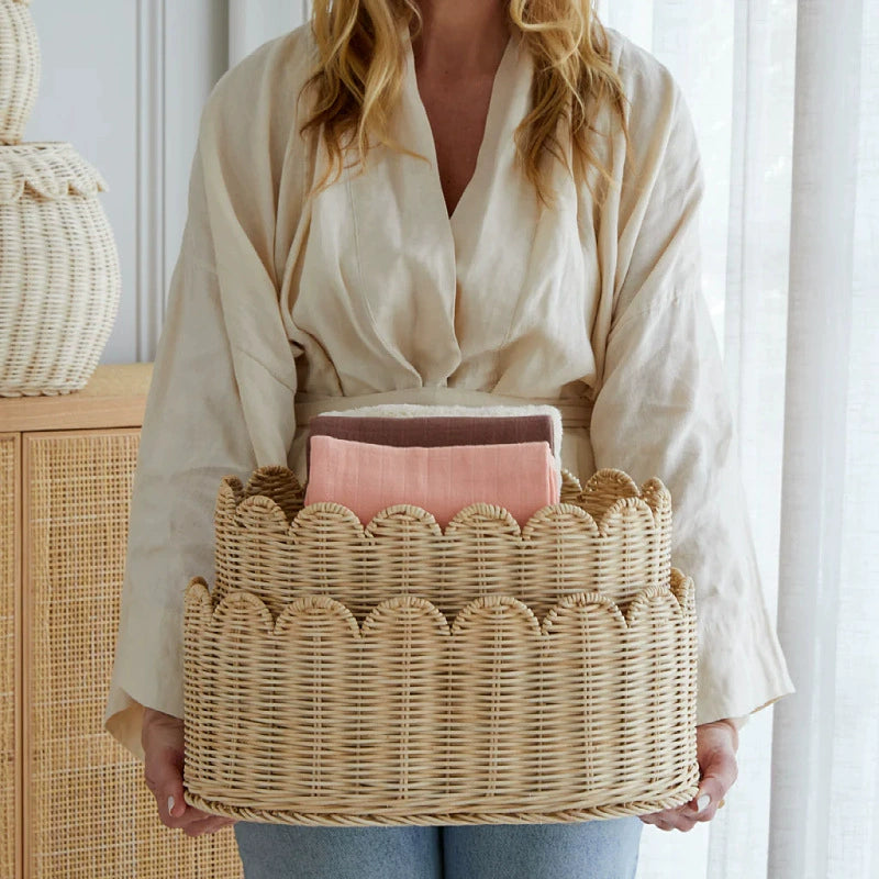 Set of 2 natural rattan wicker baskets with scalloped edges holding folded pink and brown towels.
