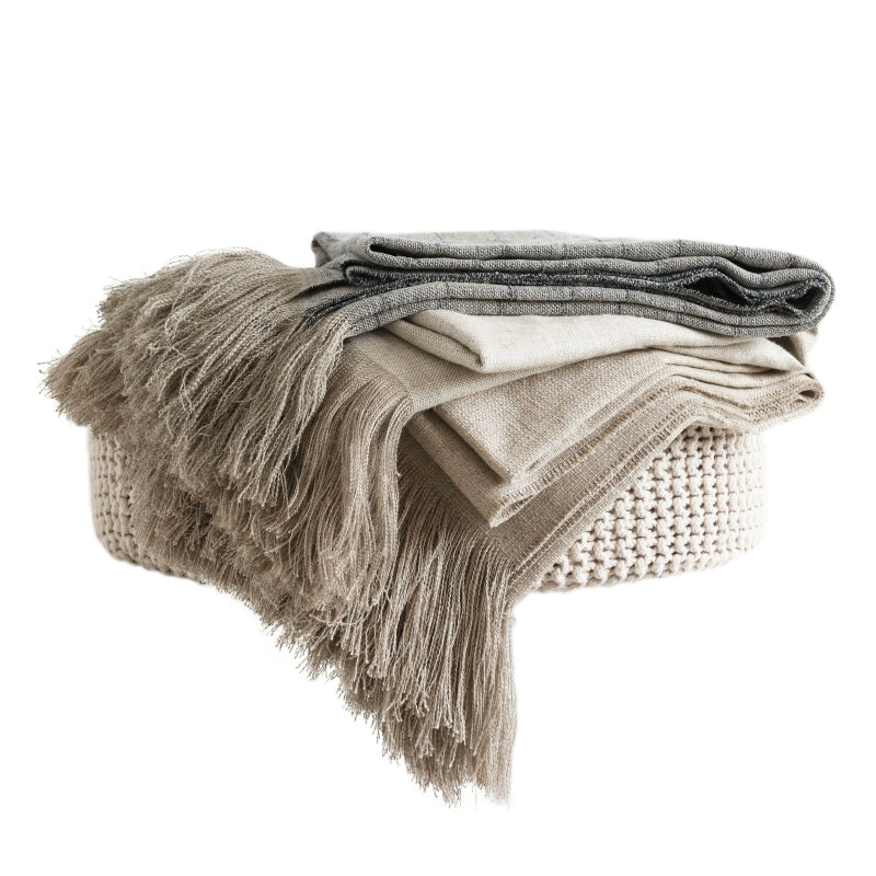 Beige linen table runner with tassels draped over woven basket, rustic decor.