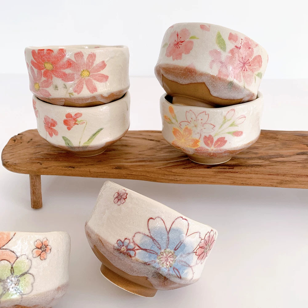 Collection of colorful, hand-painted Japanese matcha bowls stacked and displayed on a wooden stand.