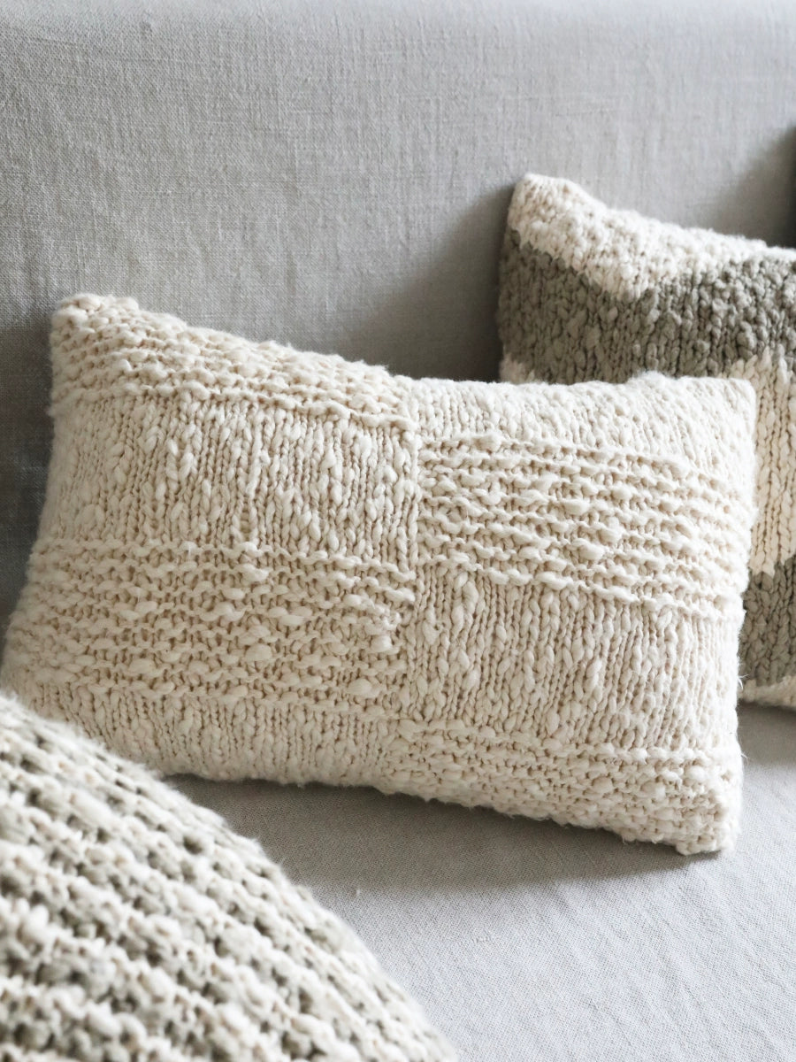 Cream and gray knitted throw pillows on a sofa, part of a cozy set.