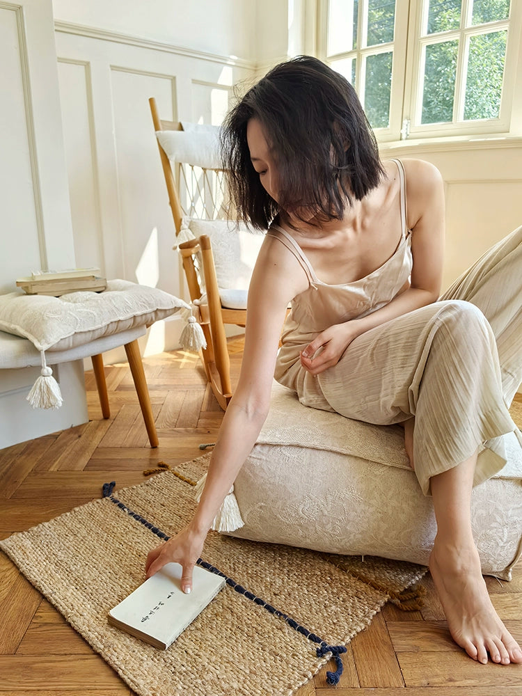 Beige embroidered ottoman pouf with tassels, decorative floor cushion on wooden floor.