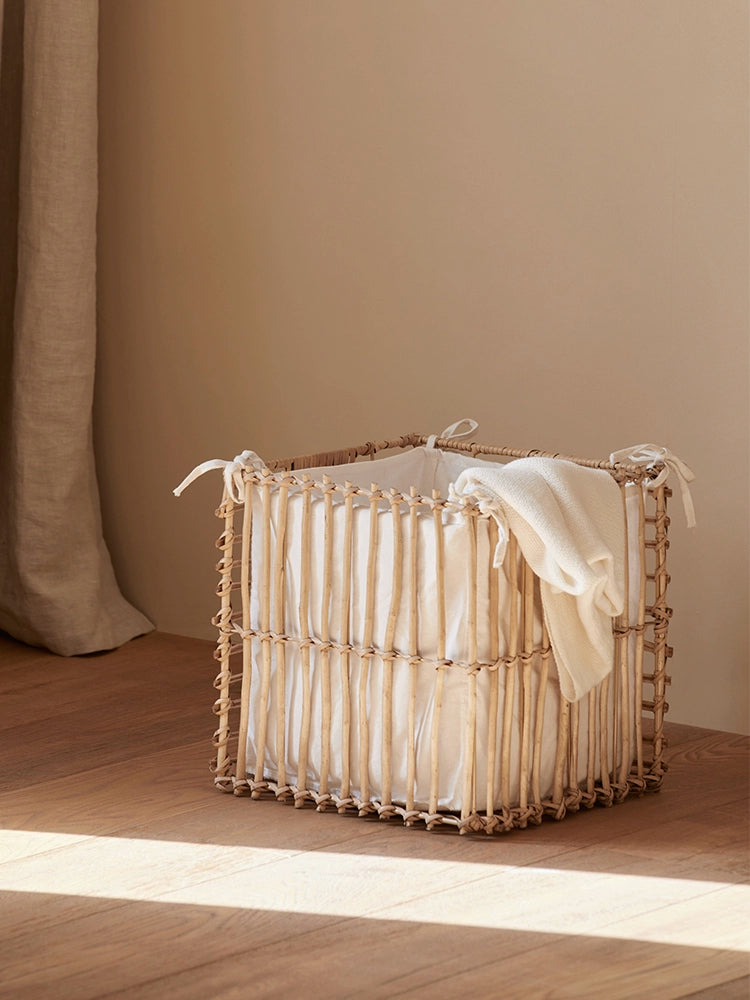 Natural rattan storage basket with white liner on wood floor, featuring a cozy blanket.