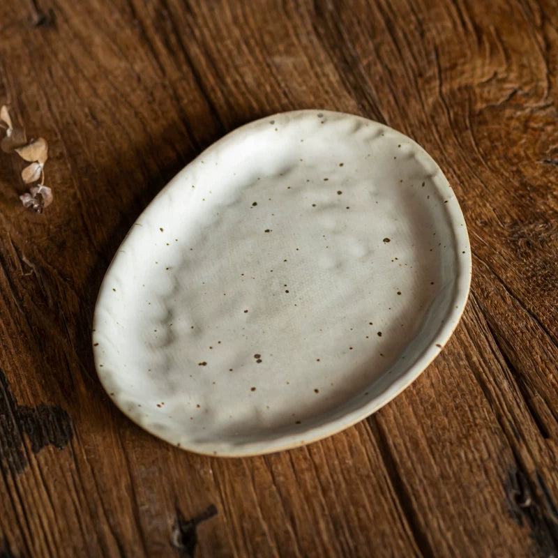 Single small, oval, speckled white ceramic plate on a dark wood grain background.