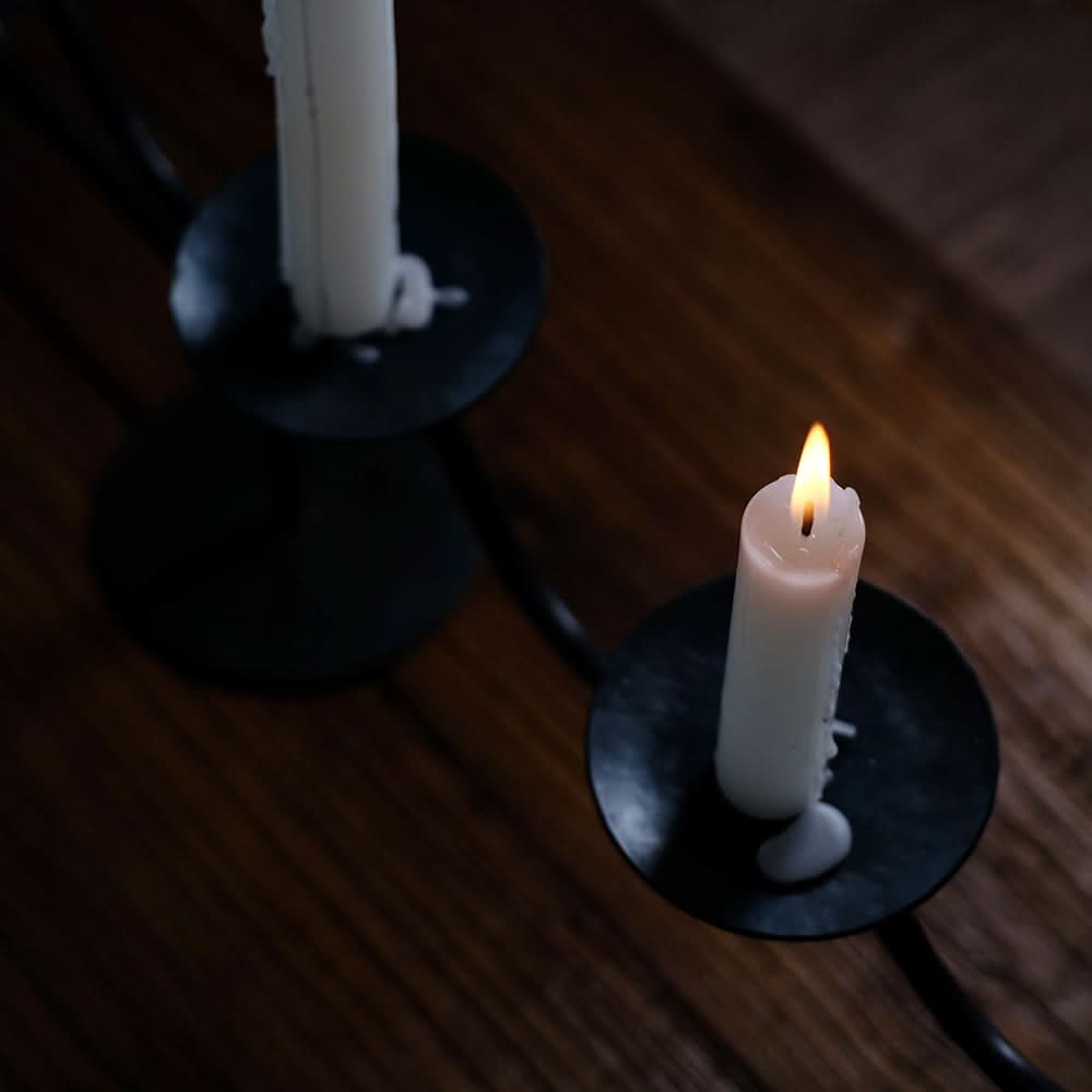 Black metal wavy Three-Candle Holder with white candles on a wooden surface.