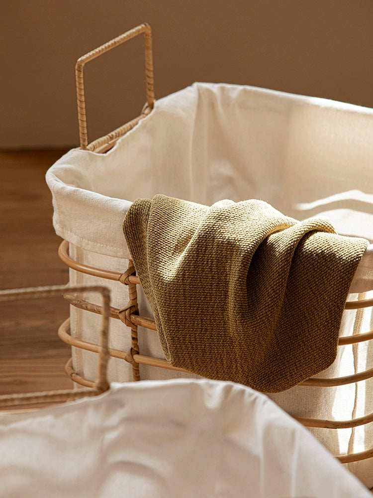 Light beige rattan laundry basket with cream linen liner;  olive green fabric draped inside.  Stylish storage.